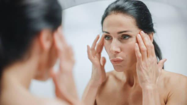Woman looking in mirror at her skin.
