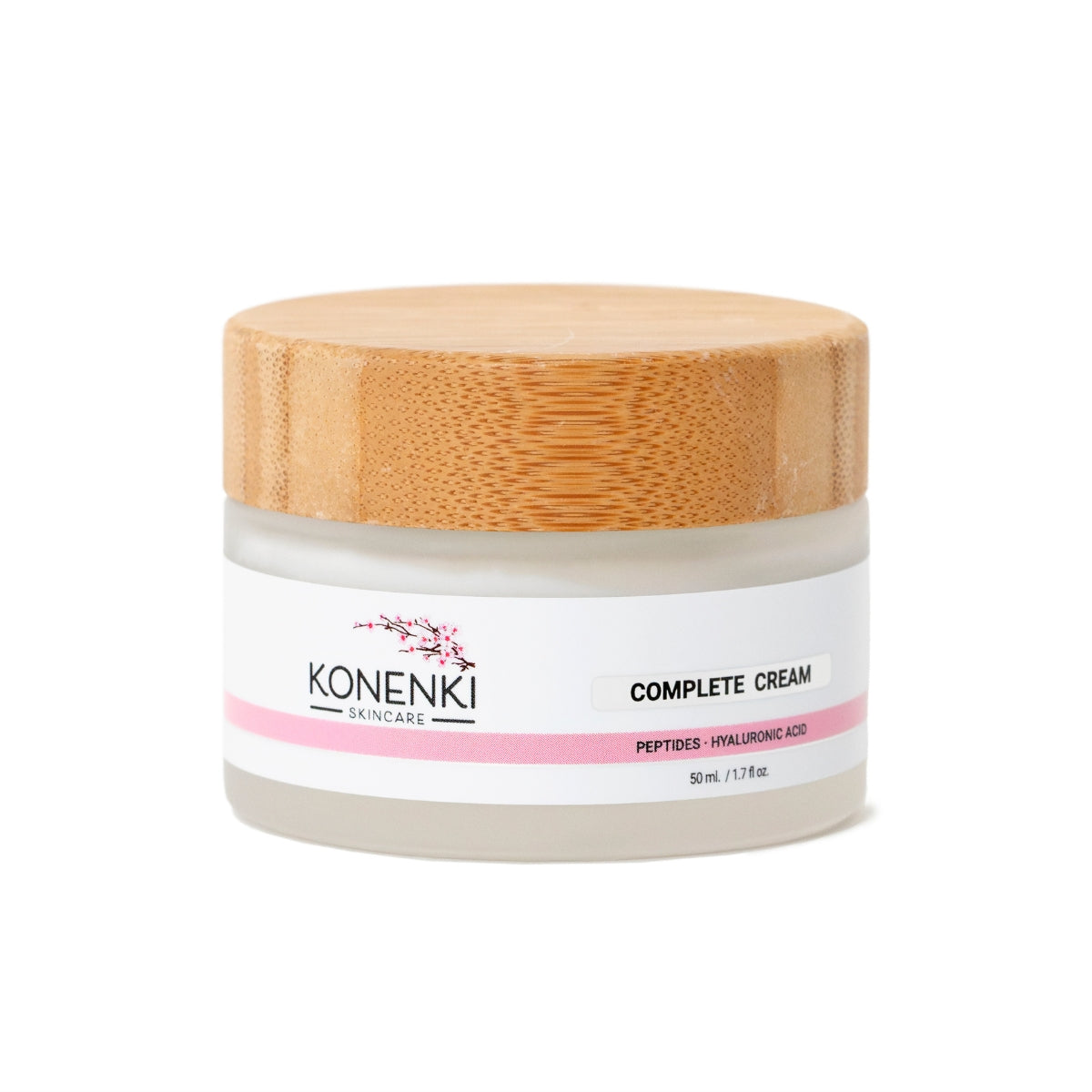 A bottle of Konenki Skincare's Complete Cream next to a pink flower against a blank white background.