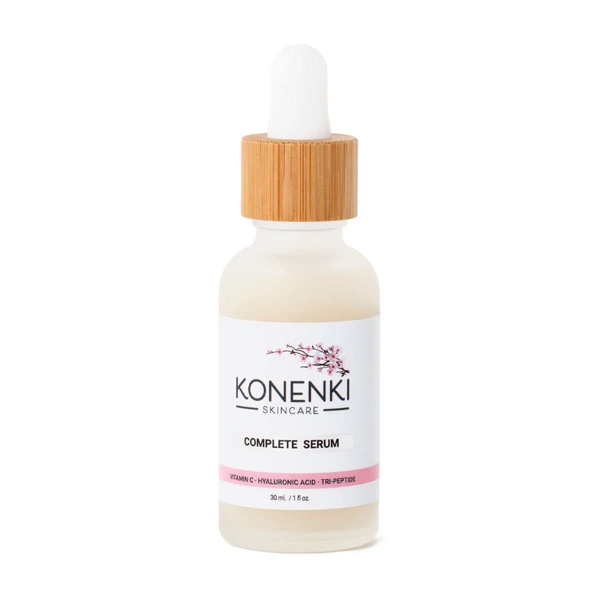 A bottle of Konenki Skincare's Complete Serum next to a pink flower against a blank white background.