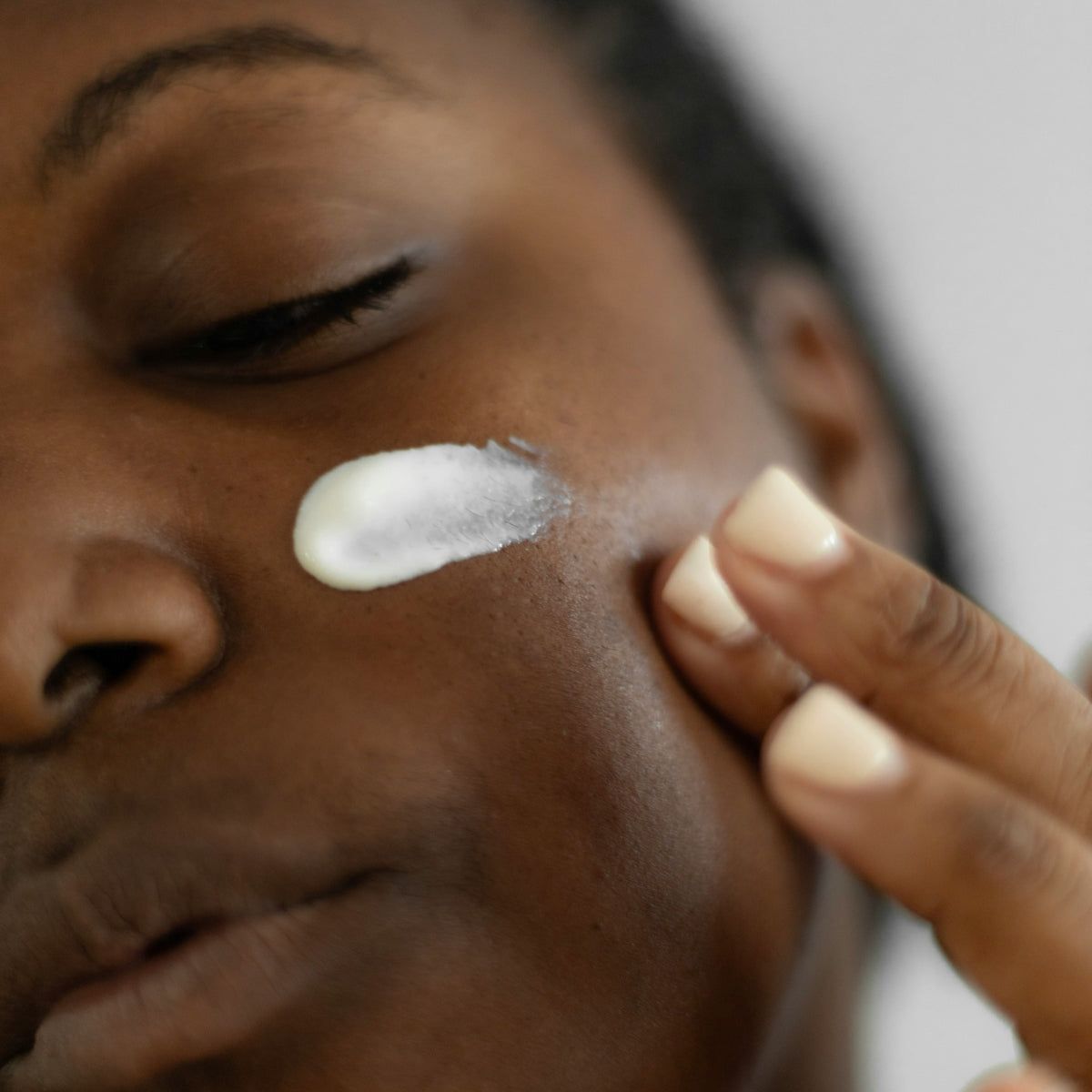 A closeup of a woman applying moisturizer to her cheek.